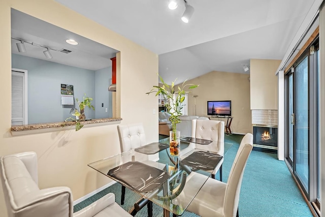 carpeted dining room with a large fireplace, lofted ceiling, and track lighting