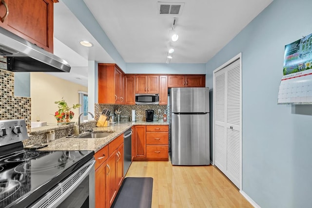 kitchen with sink, light stone counters, backsplash, appliances with stainless steel finishes, and light wood-type flooring