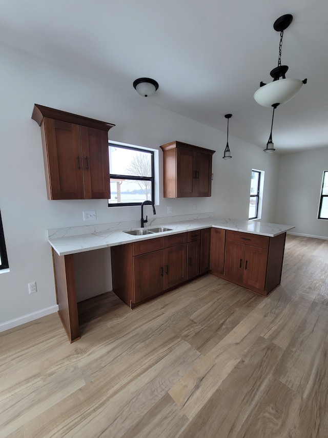 kitchen featuring light wood-style flooring, a peninsula, light countertops, pendant lighting, and a sink