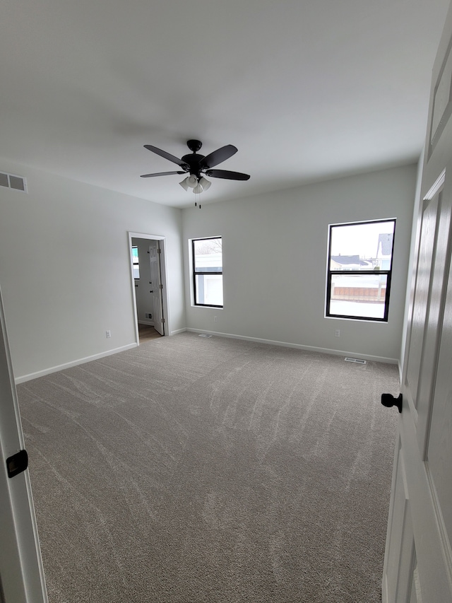 carpeted spare room with baseboards, visible vents, and ceiling fan