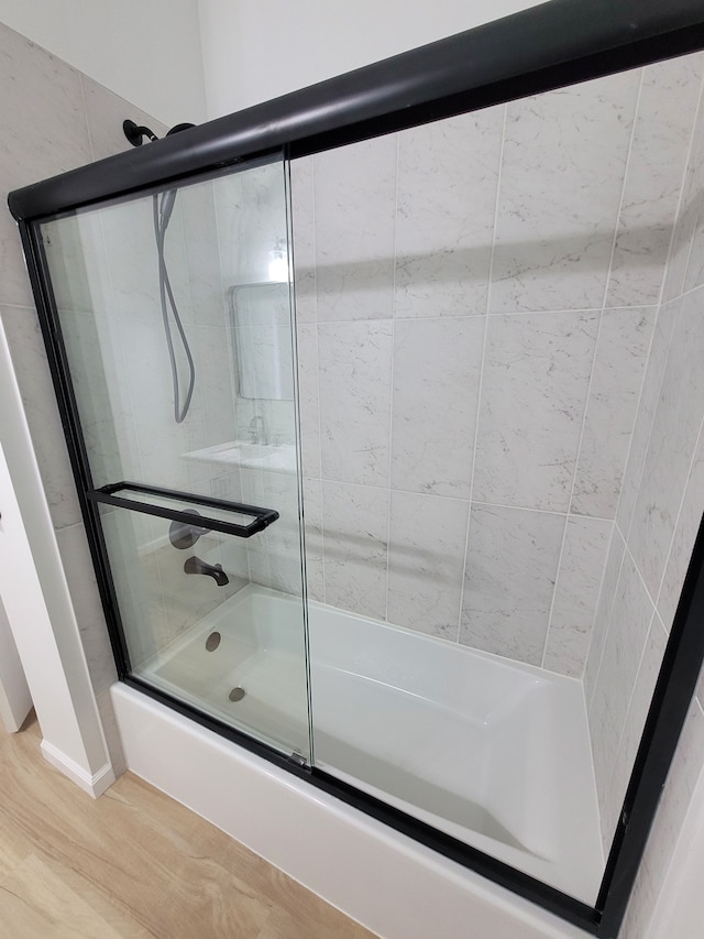 full bathroom featuring wood finished floors and bath / shower combo with glass door