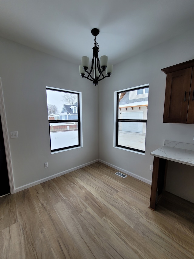 unfurnished dining area with baseboards, visible vents, a notable chandelier, and light wood finished floors