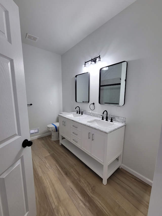 bathroom featuring toilet, double vanity, a sink, and visible vents