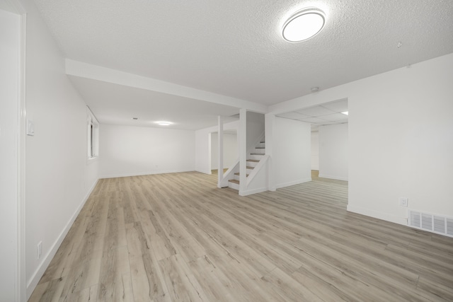 basement featuring light wood-type flooring and a textured ceiling