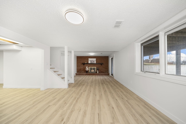 interior space with light wood-type flooring, a textured ceiling, brick wall, and a brick fireplace