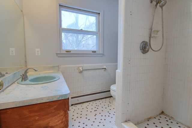 bathroom featuring vanity, baseboard heating, tiled shower, tile walls, and toilet