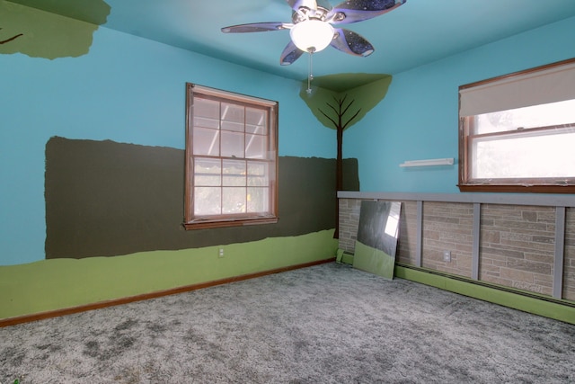 carpeted empty room with plenty of natural light, ceiling fan, and baseboard heating