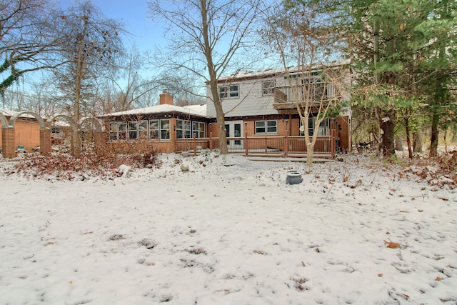 snow covered back of property with a sunroom and a wooden deck