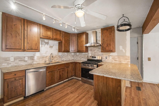 kitchen featuring kitchen peninsula, appliances with stainless steel finishes, sink, wall chimney range hood, and hardwood / wood-style flooring