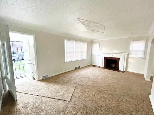 unfurnished living room with carpet flooring, a fireplace, a healthy amount of sunlight, and a textured ceiling