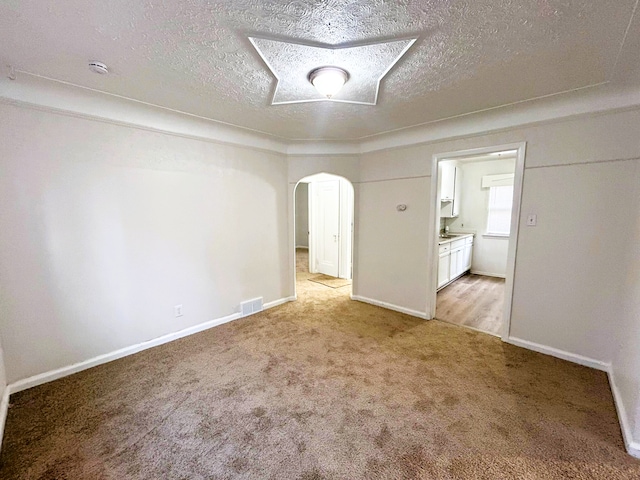 spare room with light carpet, a textured ceiling, arched walkways, and a smoke detector