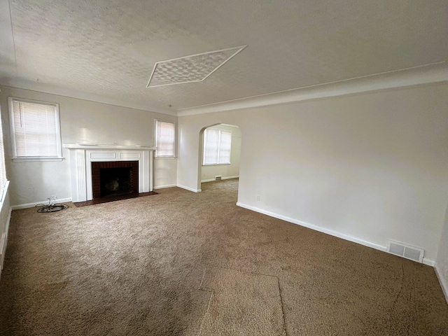 unfurnished living room featuring carpet, a healthy amount of sunlight, a textured ceiling, and a brick fireplace