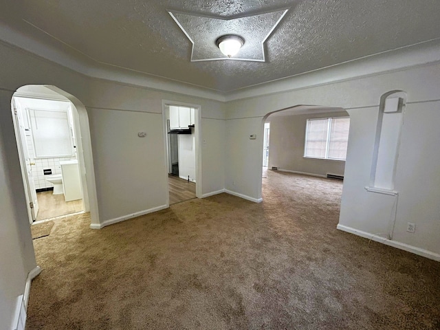 spare room with carpet flooring, a textured ceiling, arched walkways, and a baseboard heating unit
