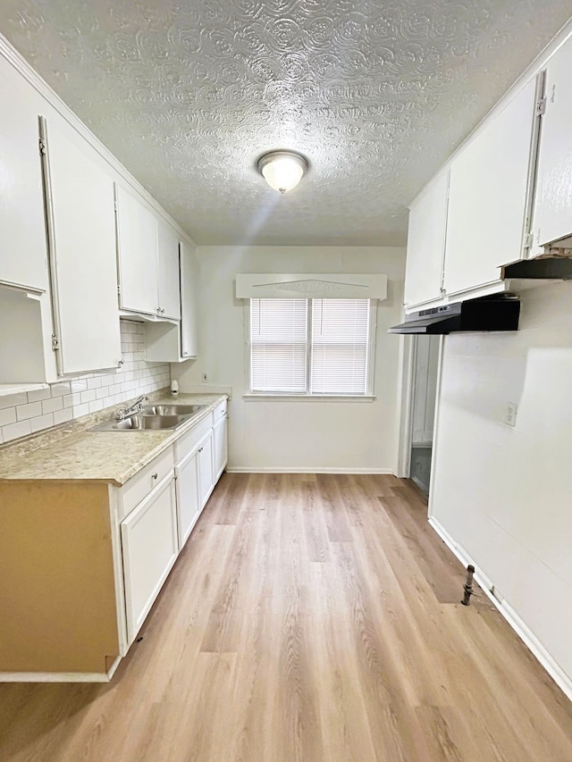 kitchen with white cabinets, decorative backsplash, light hardwood / wood-style floors, and sink