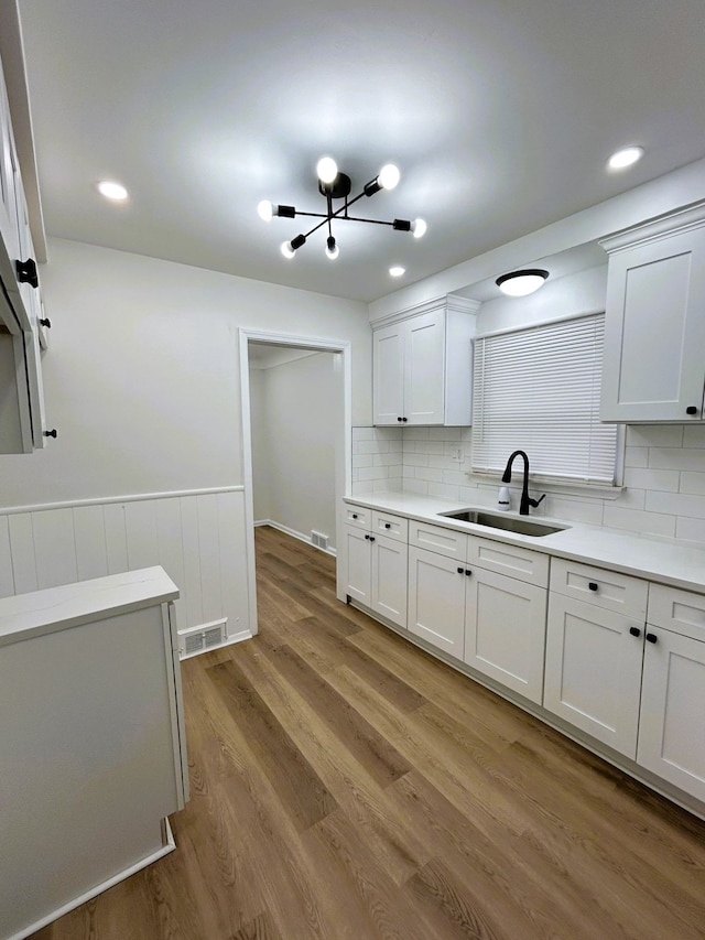 kitchen with tasteful backsplash, sink, an inviting chandelier, light hardwood / wood-style flooring, and white cabinets