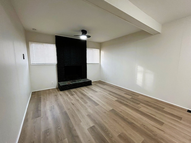 unfurnished living room with beam ceiling, a wealth of natural light, light hardwood / wood-style floors, and a brick fireplace