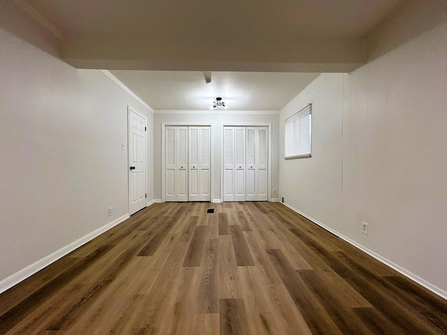 unfurnished bedroom with crown molding, hardwood / wood-style floors, and two closets