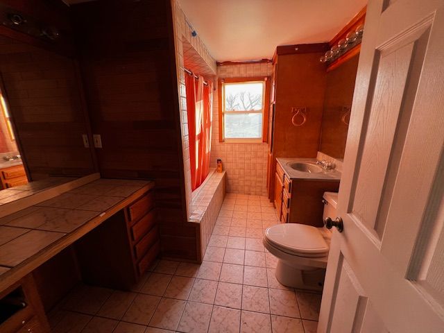 full bathroom featuring tile patterned floors, toilet, shower / bath combo with shower curtain, vanity, and tile walls