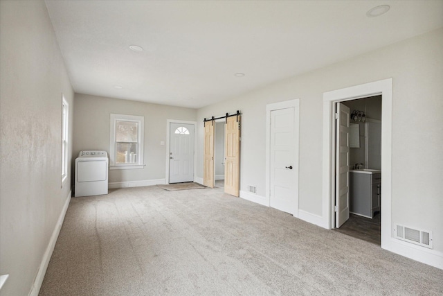 unfurnished bedroom featuring carpet flooring, washer / dryer, a barn door, and ensuite bathroom