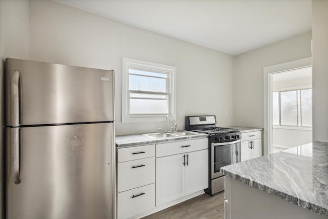 kitchen featuring white cabinetry, sink, stainless steel appliances, light stone counters, and hardwood / wood-style flooring