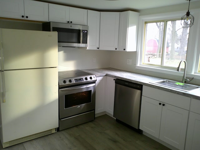 kitchen featuring sink, hanging light fixtures, white cabinetry, wood-type flooring, and stainless steel appliances