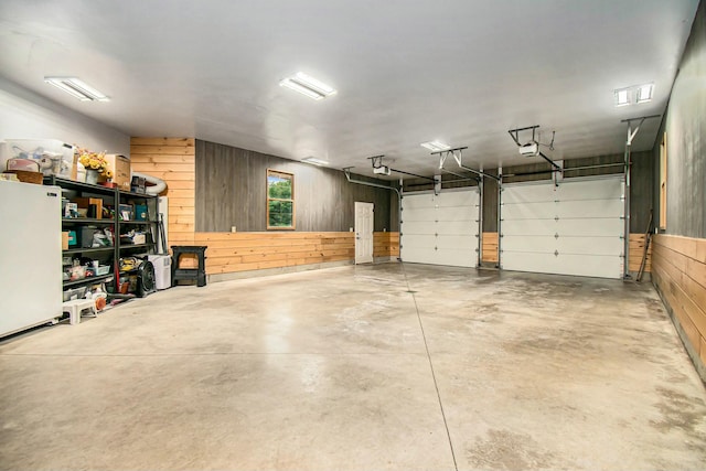 garage with wood walls, white fridge, and a garage door opener