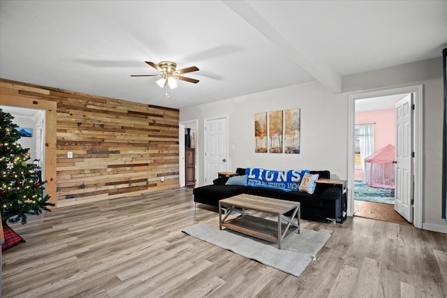 living room featuring beam ceiling, light hardwood / wood-style floors, ceiling fan, and wood walls