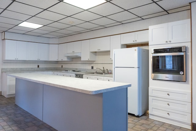 kitchen featuring white cabinetry, sink, a center island, white appliances, and a paneled ceiling