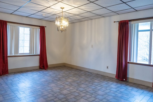 empty room with a paneled ceiling, a chandelier, and a healthy amount of sunlight