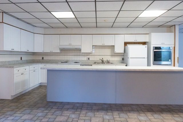 kitchen with a drop ceiling, white appliances, backsplash, sink, and white cabinetry