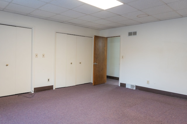 unfurnished bedroom featuring a drop ceiling, carpet floors, and two closets