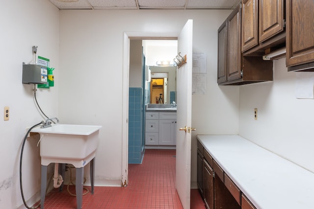 interior space with a paneled ceiling, dark tile patterned floors, and tile walls