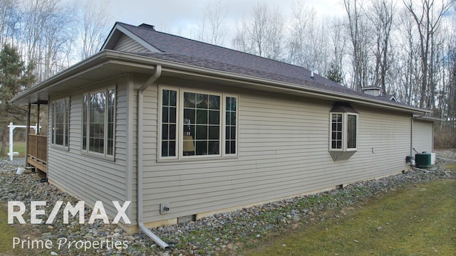 view of side of property featuring central AC unit, roof with shingles, and crawl space