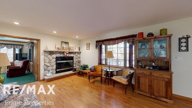 living area featuring recessed lighting, baseboards, a stone fireplace, and light wood-style flooring