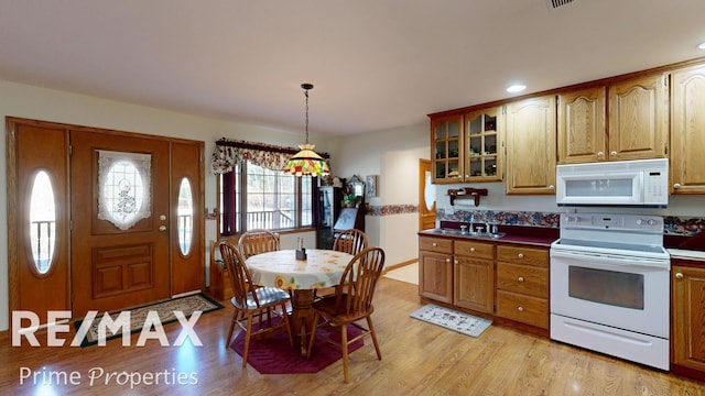 kitchen featuring a sink, white appliances, light wood-style floors, brown cabinetry, and glass insert cabinets