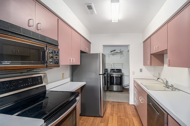 kitchen featuring independent washer and dryer, sink, light hardwood / wood-style floors, and appliances with stainless steel finishes