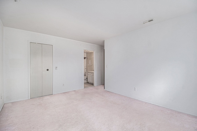 unfurnished bedroom with light carpet, ensuite bathroom, and a closet