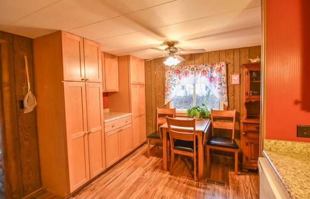 dining area with ceiling fan, wooden walls, and light hardwood / wood-style flooring