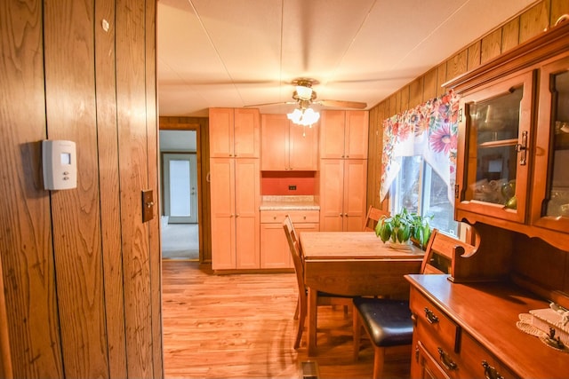 dining room featuring light hardwood / wood-style floors, ceiling fan, and wooden walls