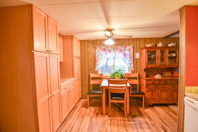 dining room with ceiling fan, wood walls, and light hardwood / wood-style floors