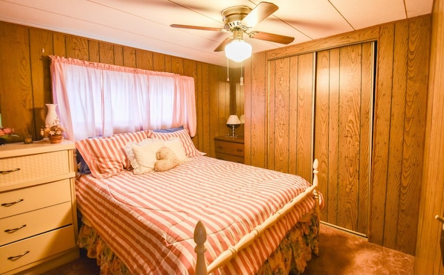 bedroom with ceiling fan, wood walls, and dark colored carpet