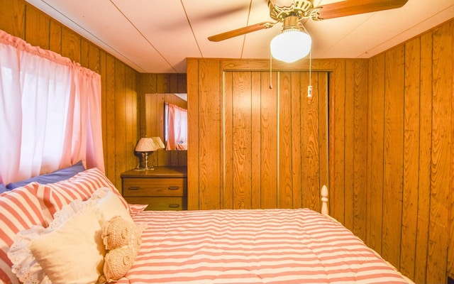 bedroom with ceiling fan and wooden walls