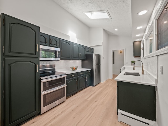 kitchen with sink, a skylight, a textured ceiling, appliances with stainless steel finishes, and light hardwood / wood-style floors