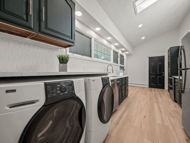 washroom with a textured ceiling, baseboard heating, sink, light hardwood / wood-style flooring, and washing machine and dryer