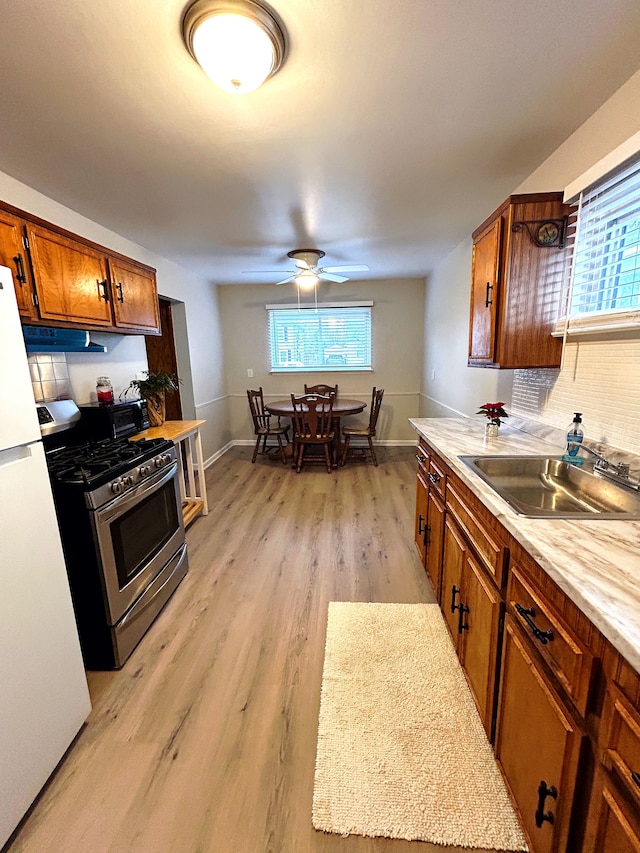 kitchen featuring sink, stainless steel gas range, light hardwood / wood-style floors, tasteful backsplash, and white fridge