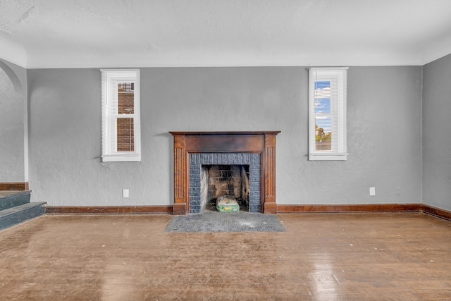 unfurnished living room with wood-type flooring and a brick fireplace