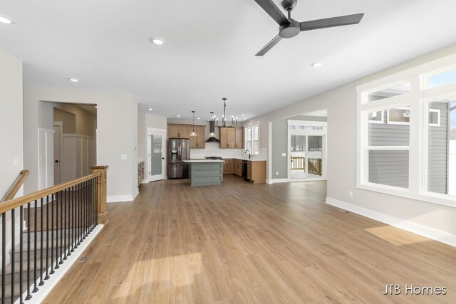 unfurnished living room with recessed lighting, ceiling fan with notable chandelier, a sink, baseboards, and light wood-type flooring