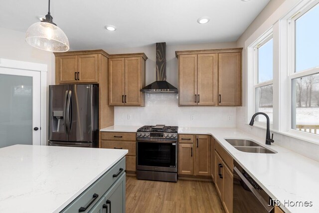 kitchen featuring stainless steel appliances, a sink, wall chimney range hood, tasteful backsplash, and decorative light fixtures