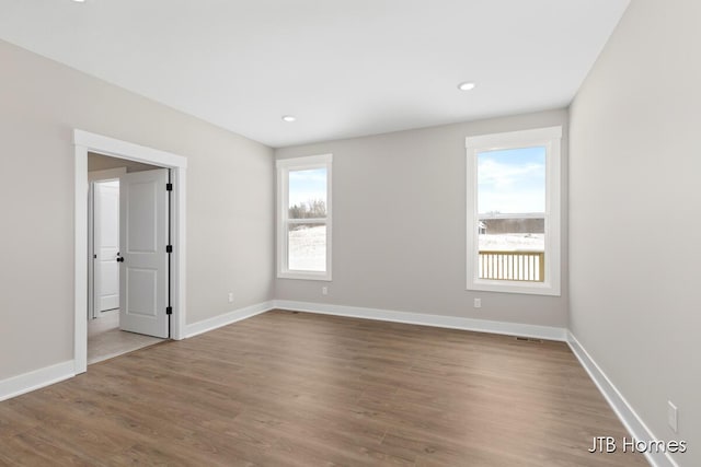 empty room featuring baseboards, recessed lighting, wood finished floors, and a healthy amount of sunlight