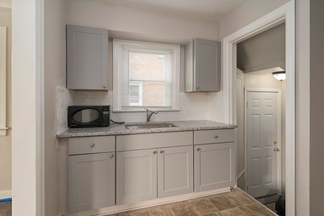 kitchen featuring tasteful backsplash, gray cabinetry, light stone countertops, and sink